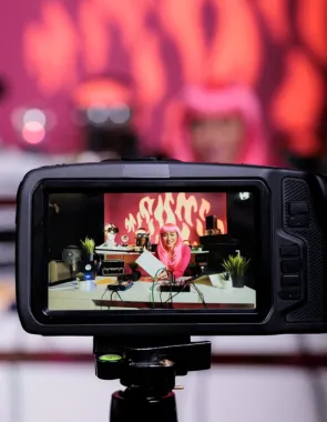 A video camera captures a female social media influencer in a pink outfit while she gets filmed.